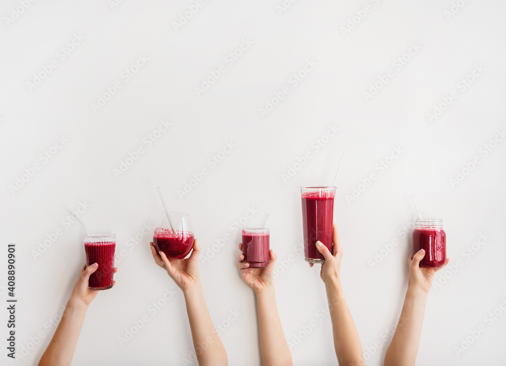 Multiple hands holding glasses with Purple beet and pomegranate fresh smoothie with glass straws, wh