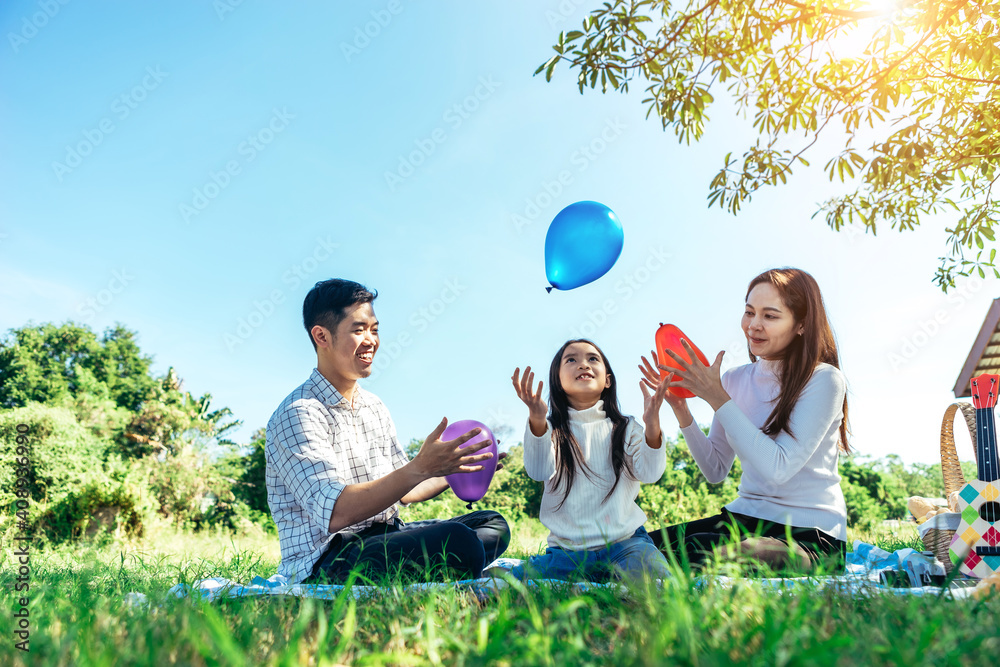 快乐的亚洲家庭在花园里野餐，一起快乐地玩彩色气球。