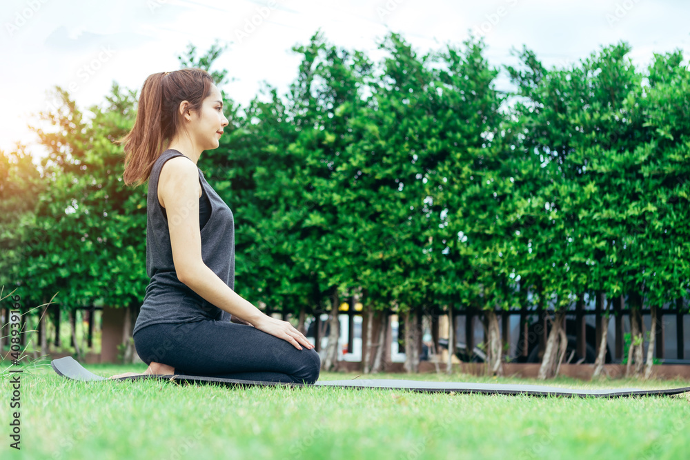放松健康运动穿着健身服的亚洲女性在公园冥想，使用在线流媒体瑜伽