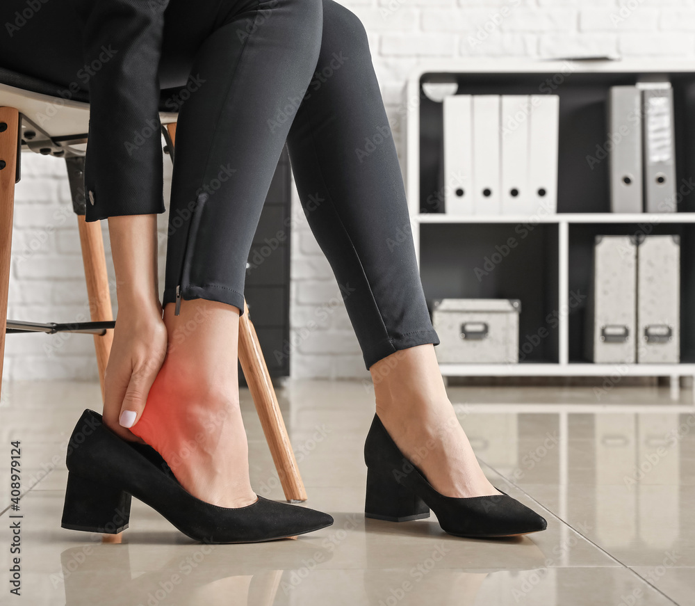 Young woman feeling ache because of wearing uncomfortable shoes in office