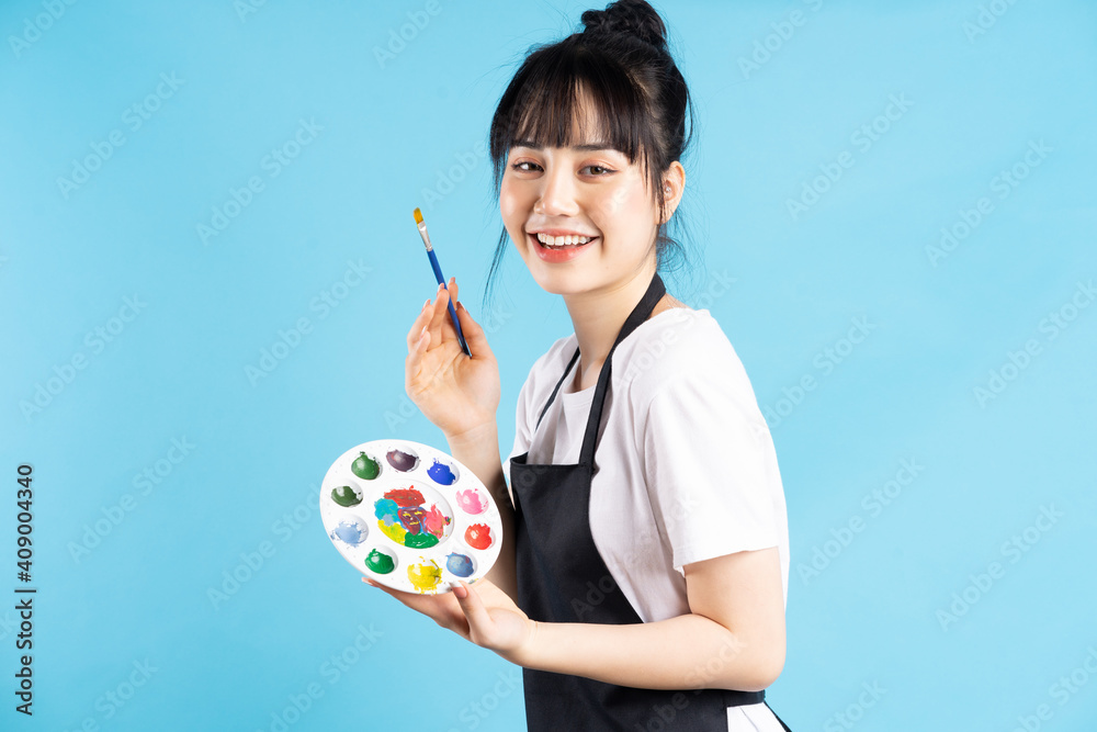 美丽的亚洲女画家拿着羽毛笔和蓝色背景的调色板
