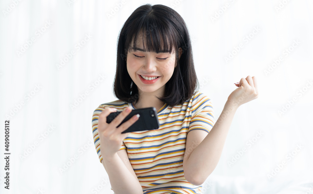 漂亮的亚洲女人在卧室用智能手机玩游戏