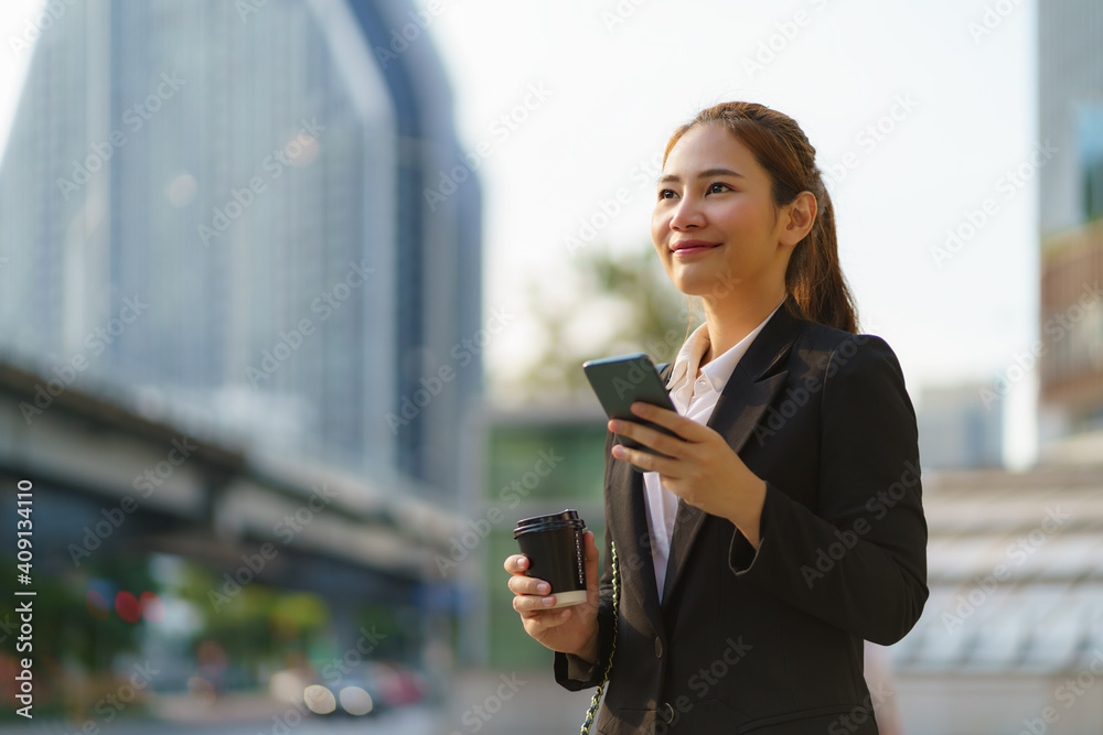 亚洲高管职场女性拿着咖啡杯在办公室的街道上使用手机