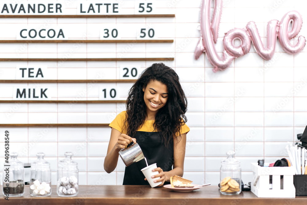 穿着黑色围裙的快乐非洲裔美国女咖啡师站在酒吧柜台边煮咖啡，