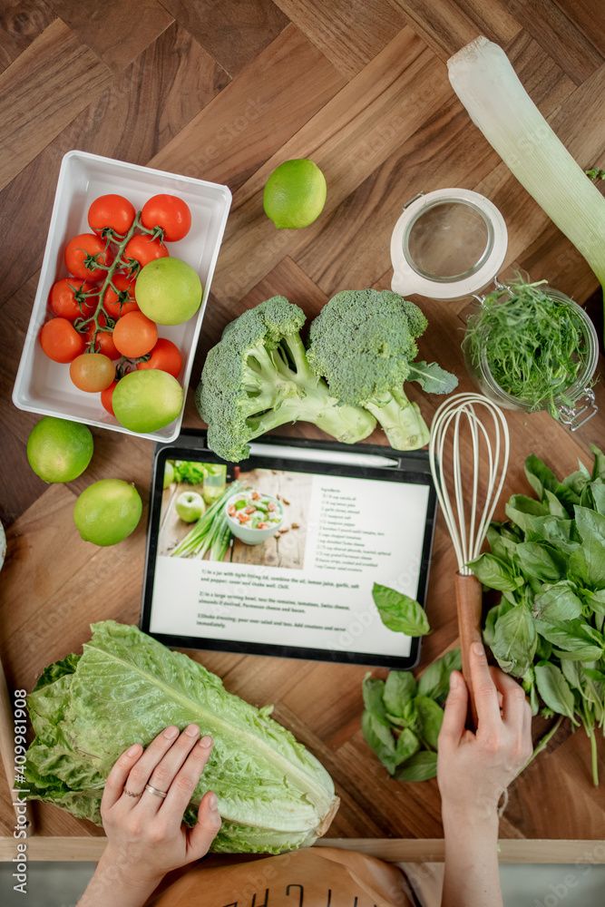 餐桌上的数字平板电脑上的健康沙拉食谱，配绿色蔬菜和女人的手。H