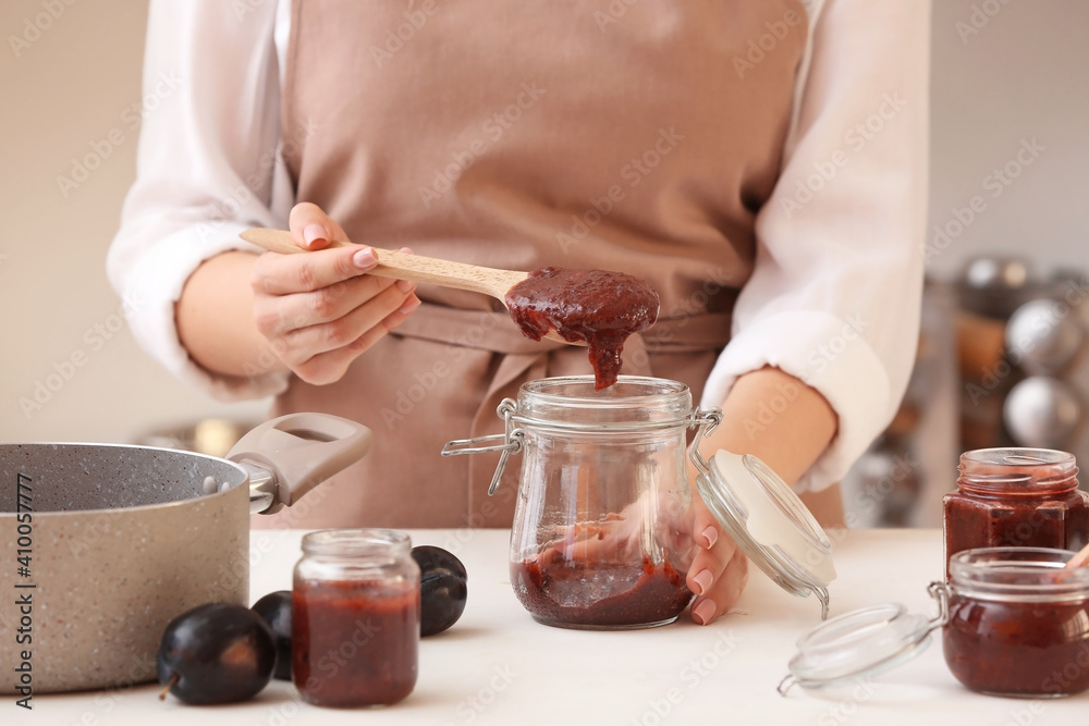 Woman pouring delicious homemade plum jam into jar