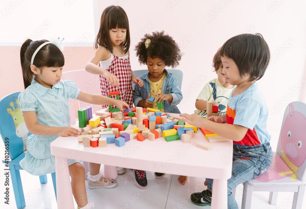 一群多元化的孩子在幼儿园的课堂上玩桌子上的彩色积木。幼儿园