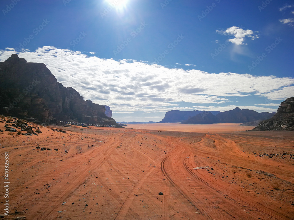 a valley in the Wadi Rum desert with car tracks, a tourist camp at the foot of the mountain, a sunny