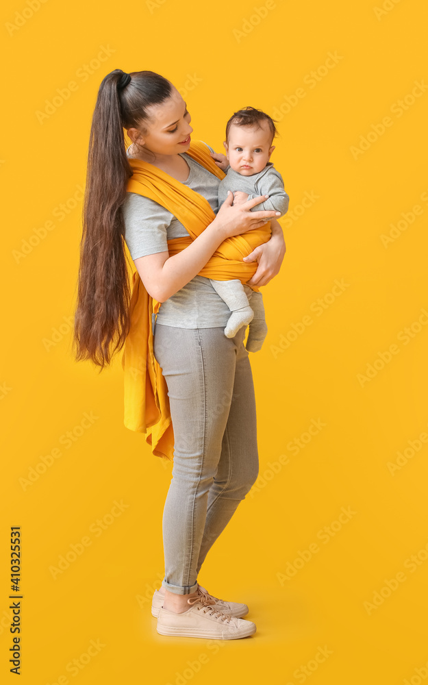 年轻的母亲带着小婴儿穿着彩色背景的吊带