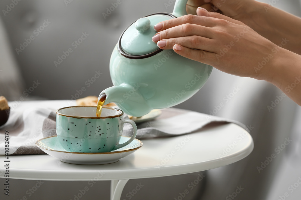 女人把茶壶里的茶倒进房间桌子上的杯子里