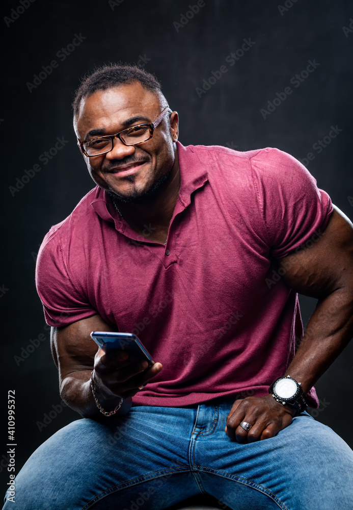 Smiling black young muscular man in pink shirt with phone in hands. Cheerful african american with b