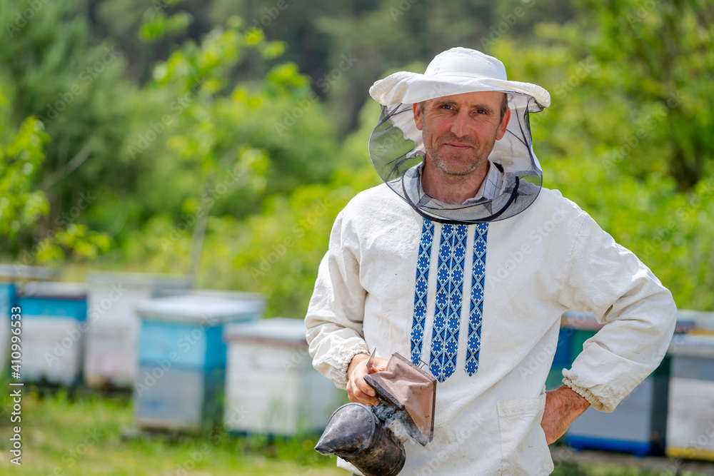 养蜂场里，认真工作的养蜂人对着镜头摆姿势。手里拿着蜜蜂吸烟者的男人。养蜂