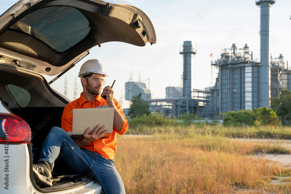 炼油厂工程师坐在车上，用笔记本电脑对着炼油厂的背影