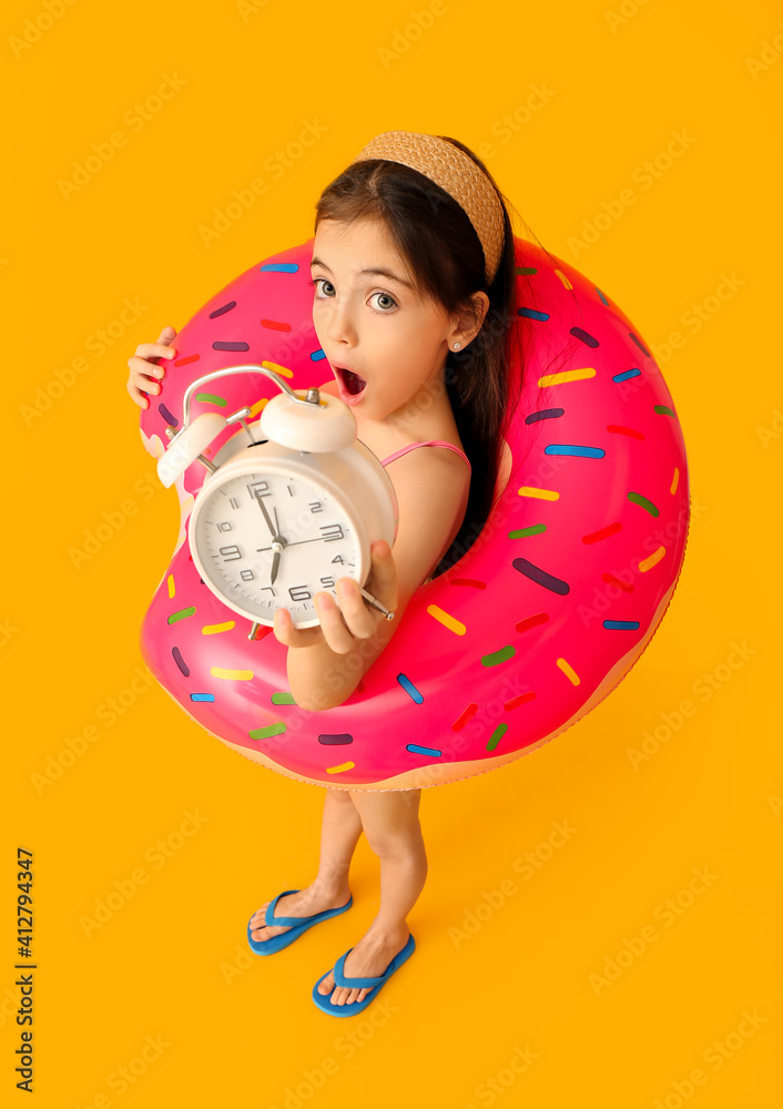 Surprised little girl in swimsuit, with alarm clock and inflatable ring on color background