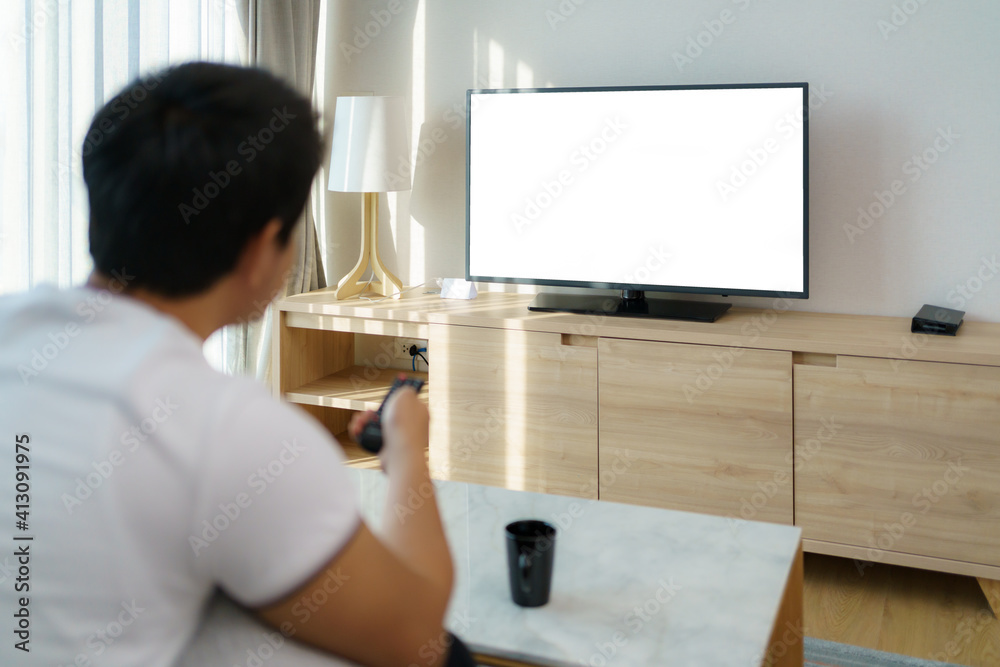 一名亚洲男子拿着电视遥控器，在沙发上看电视时按下频道。