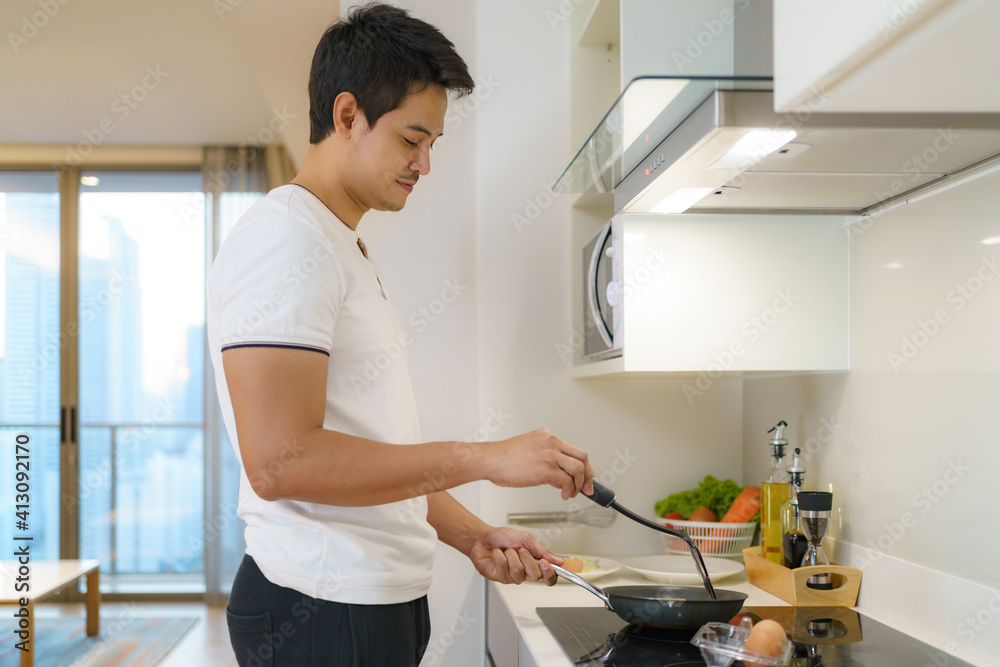 一名亚裔男子在家里的厨房里用煎蛋做美式早餐。