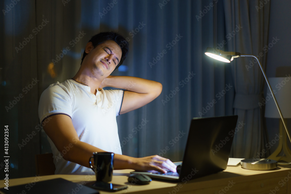 Asian man are stretch lazily while working long hours in front of a computer in late night in living