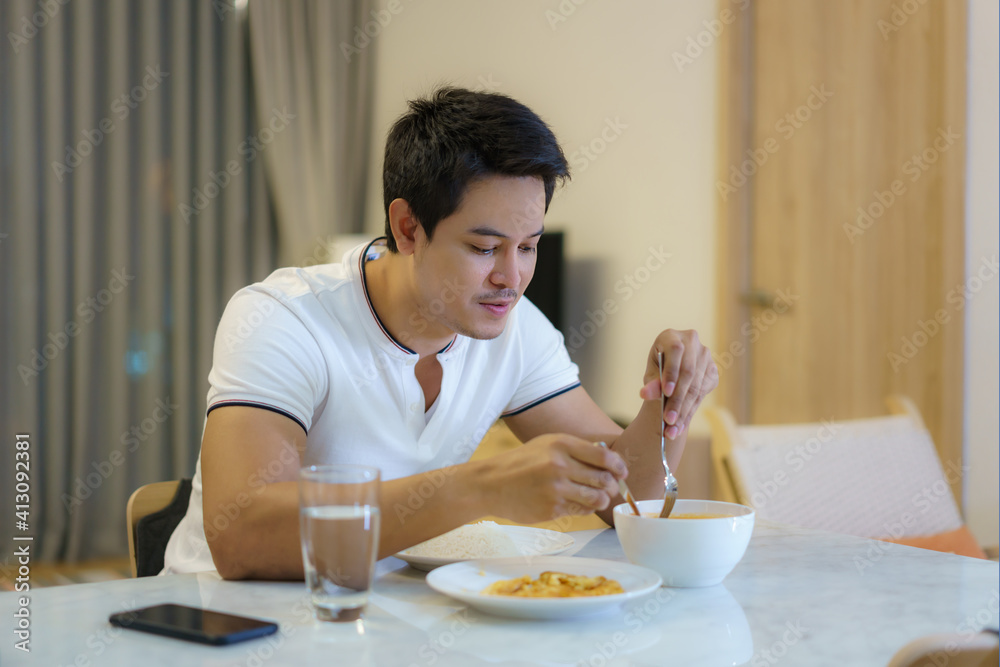 一名亚裔男子晚上独自在家的餐桌上吃晚饭。