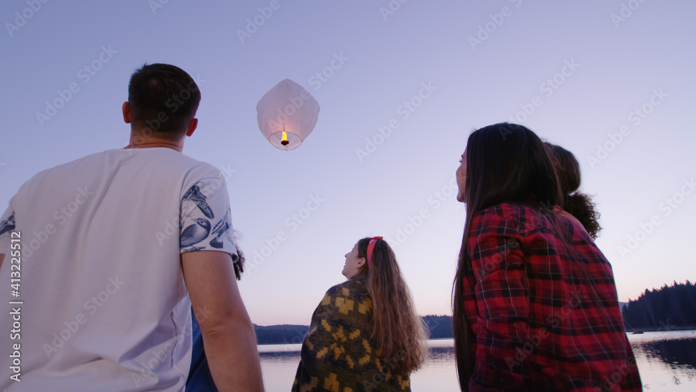 Diverse Group Of Young Men And Women Holding A Sky Lantern Smiling And Releasing it Camping Youth To