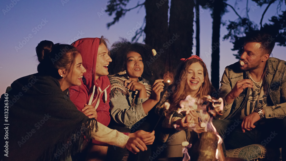 一群快乐的朋友晚上在森林里露营，笑着抱着棉花糖自然之旅