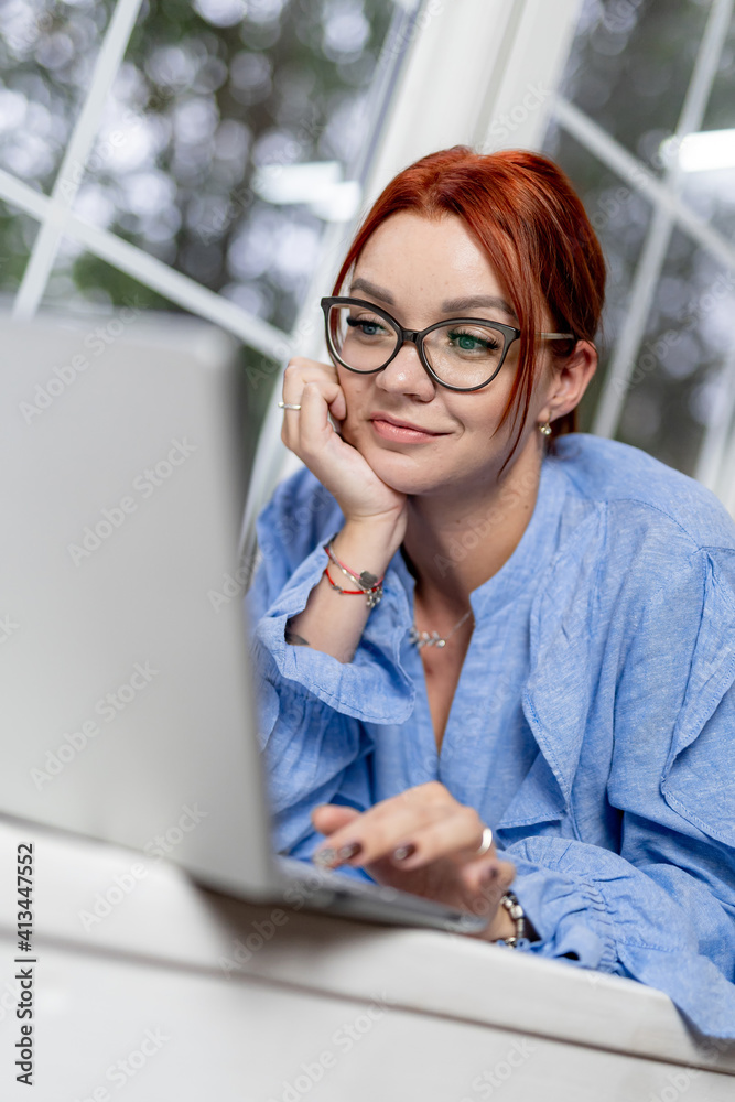 一名妇女面带微笑，躺在木制平台上使用笔记本电脑。在家里工作