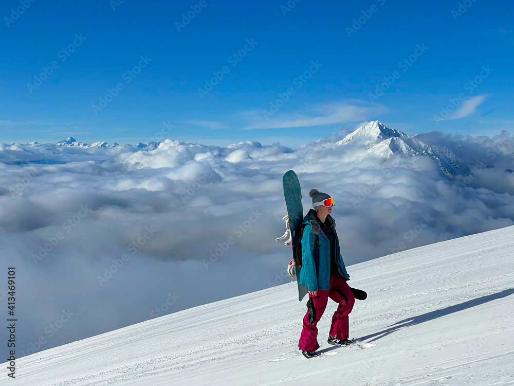 Young woman snowboarding in closed Krvavec ski resort hikes up a groomed slope.