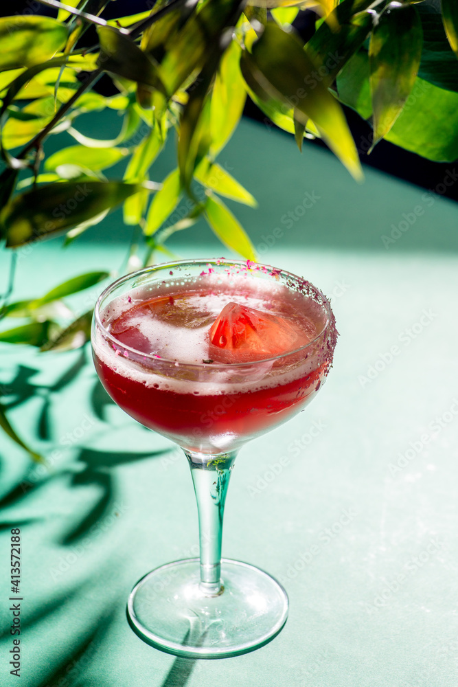 红色热带鸡尾酒，在树叶和阴影的背景上以水晶的形式加入冰块