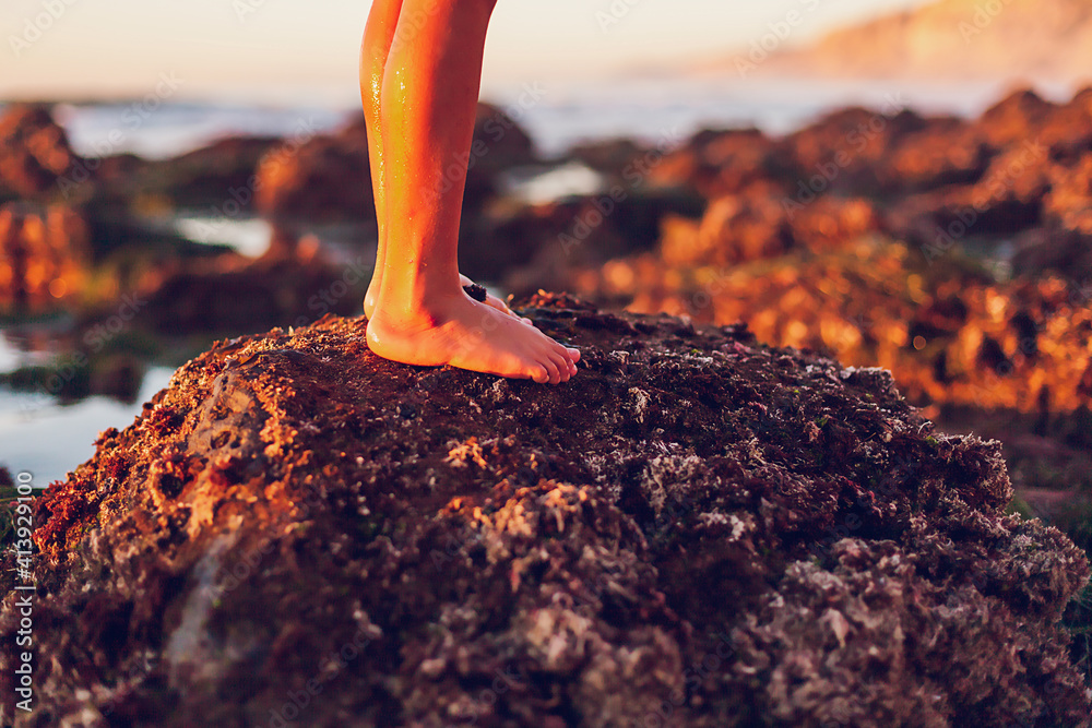 退潮时，男孩站在海滩的岩石上，专注于双脚。