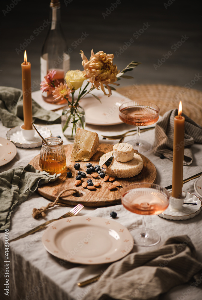 浪漫的餐桌设置，家庭封锁派对概念。瓶装和玻璃杯中的玫瑰酒，奶酪板，