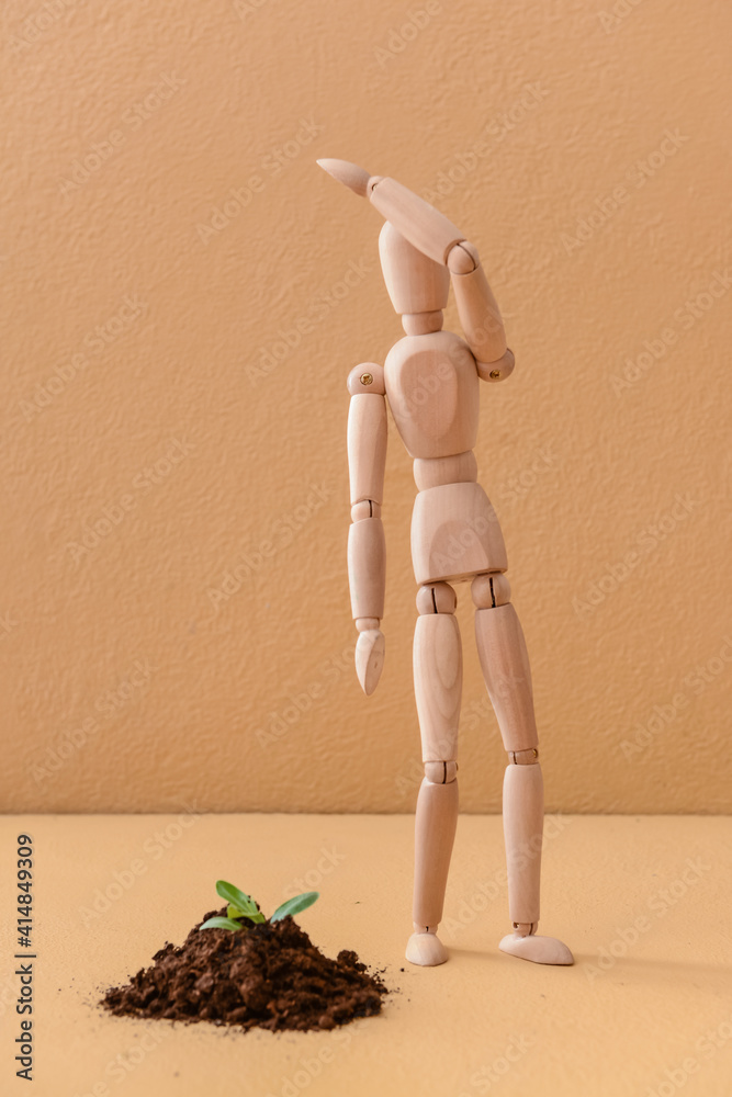 Wooden mannequin with plant in ground on color background