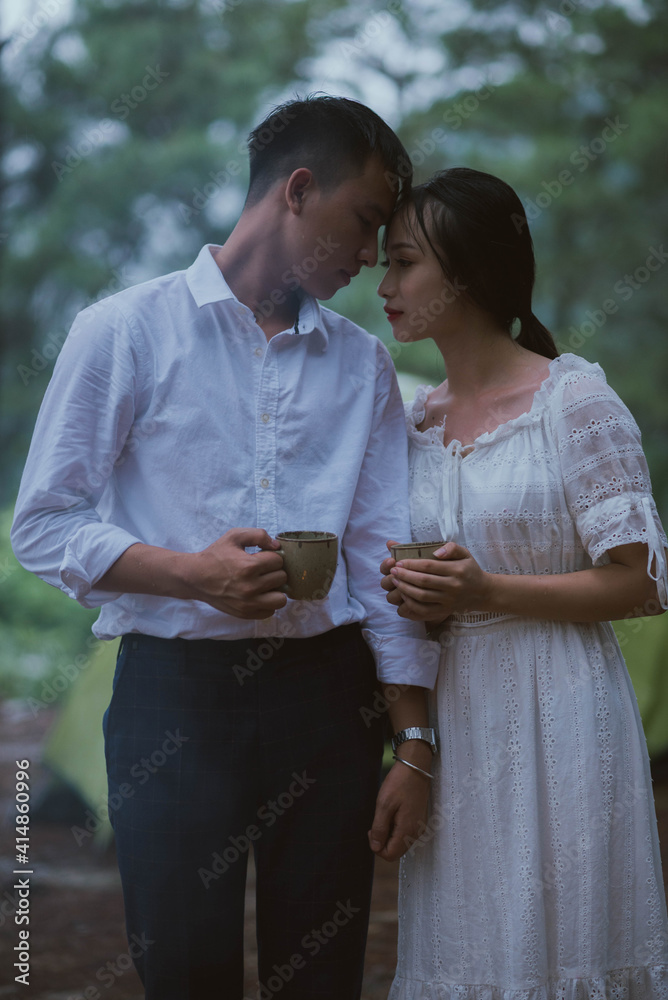 A shot of a young Asian couple drinking coffee in the evening while camping in the woods
