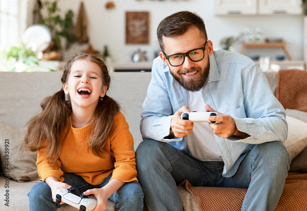 父亲和女儿一起使用电子游戏机大笑和玩电子游戏