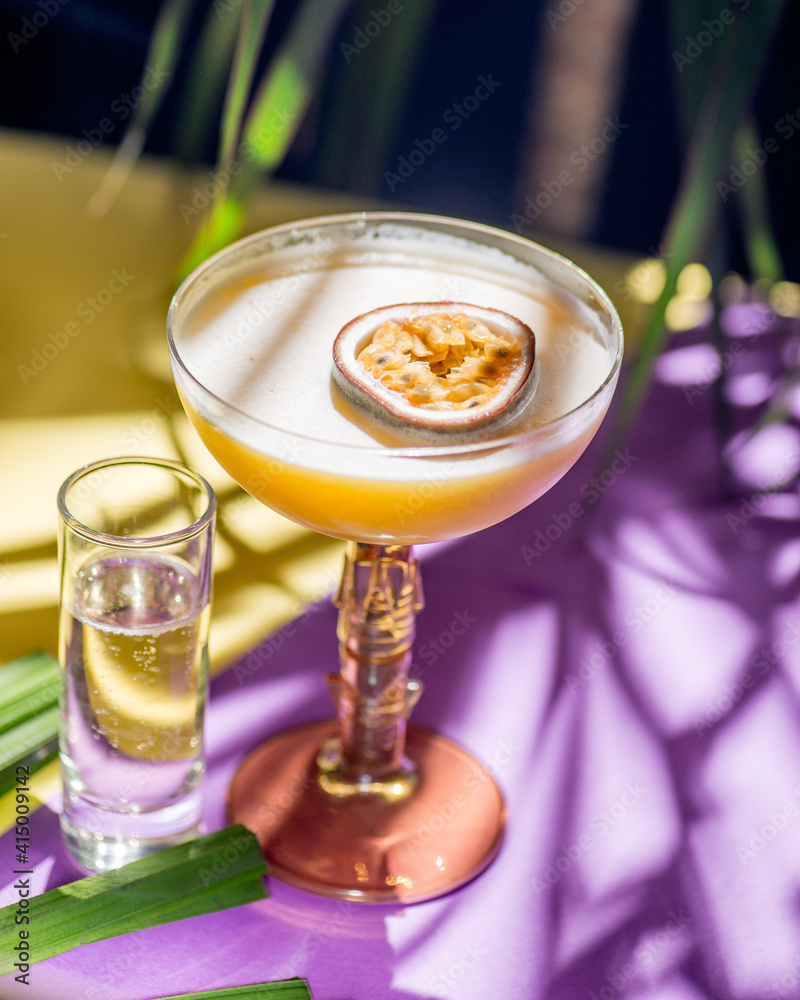 黄色热带鸡尾酒配百香果，以热带植物叶子和苏为背景拍摄