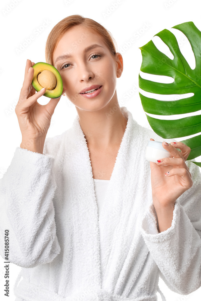 Beautiful young woman with facial cream, avocado and tropical leaf on white background