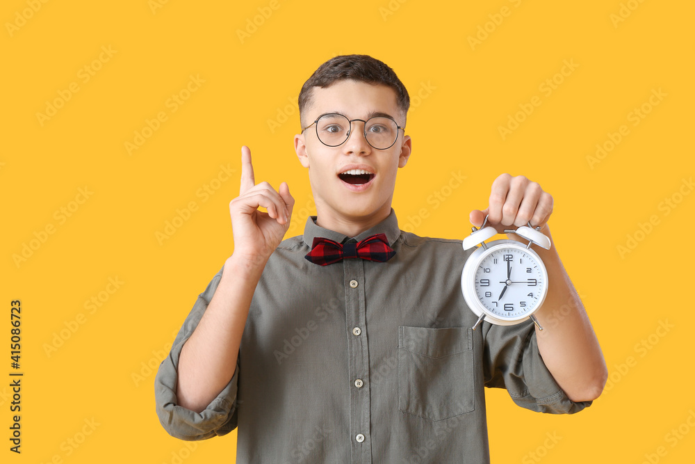 Teenager with alarm clock and raised index finger on color background