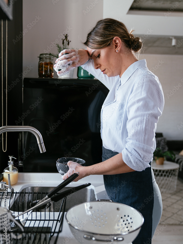 美丽的年轻女人在厨房水槽洗碗。厨房里快乐的微笑女人
