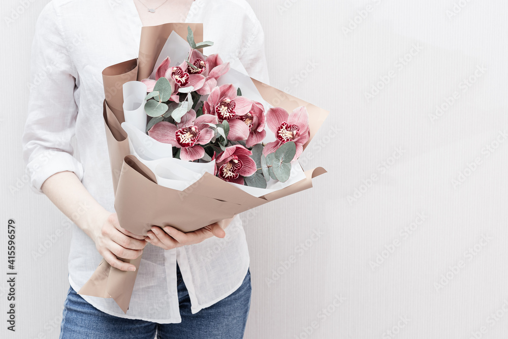 Blossoming delicate flowers of pink orchid in hands of female on light background. Modern bouquet to