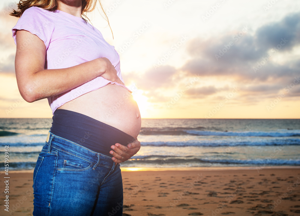 一名孕妇在沙滩度假时的近照，日落时抚摸腹部