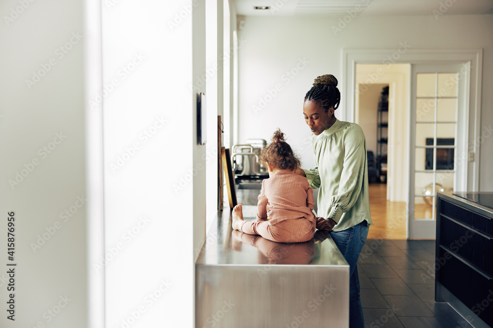 妈妈站在厨房里，她的小女儿坐在柜台上