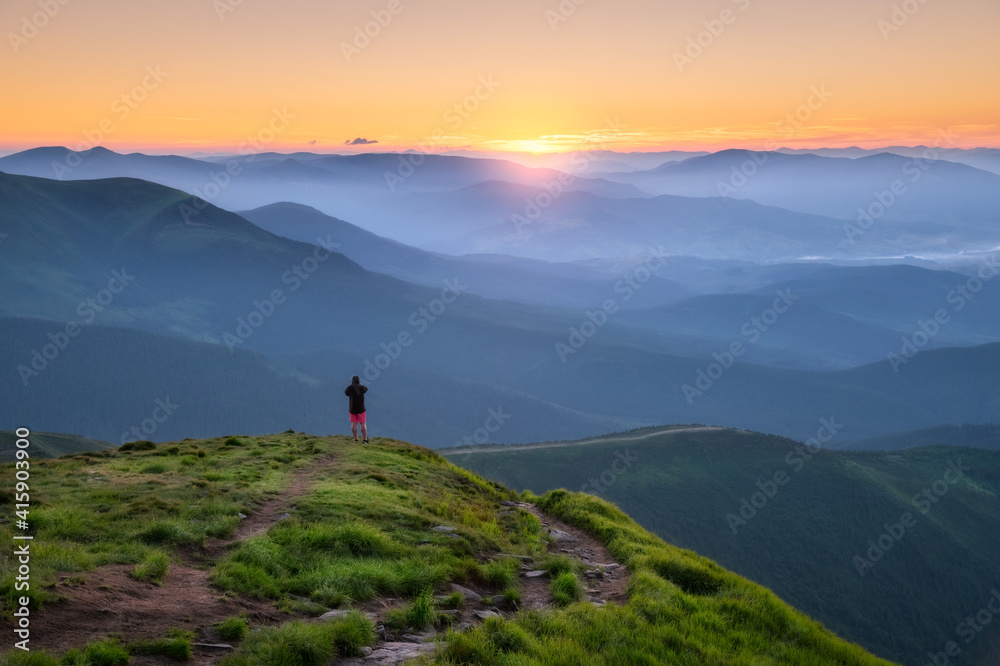 山峰上的运动型男子在summe的彩色日落中用阳光眺望山谷