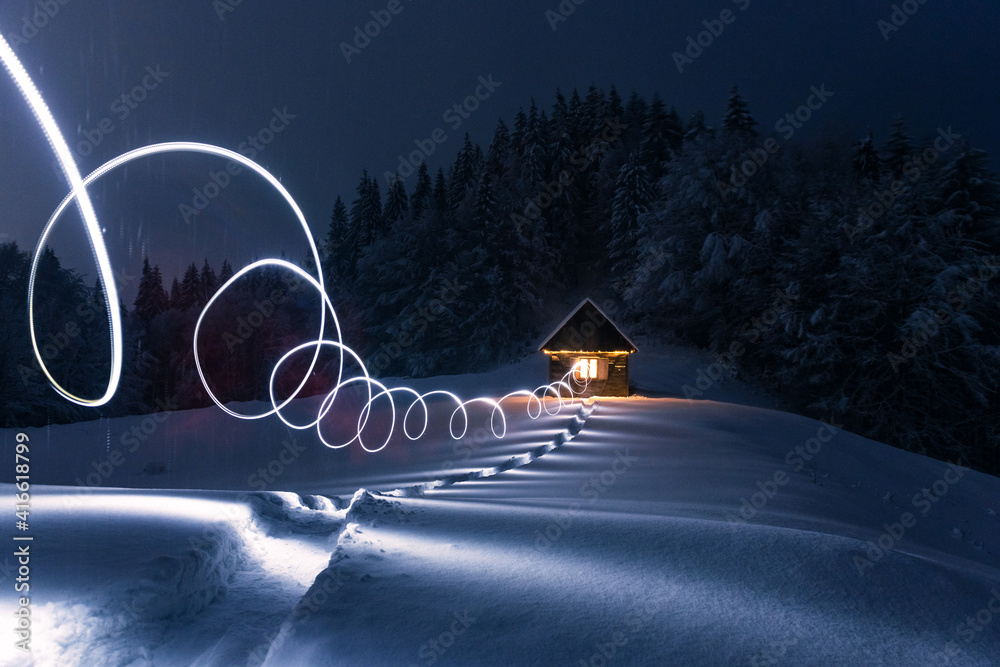 Fantastic winter landscape with glowing wooden cabin in snowy forest. Cozy house in Carpathian mount