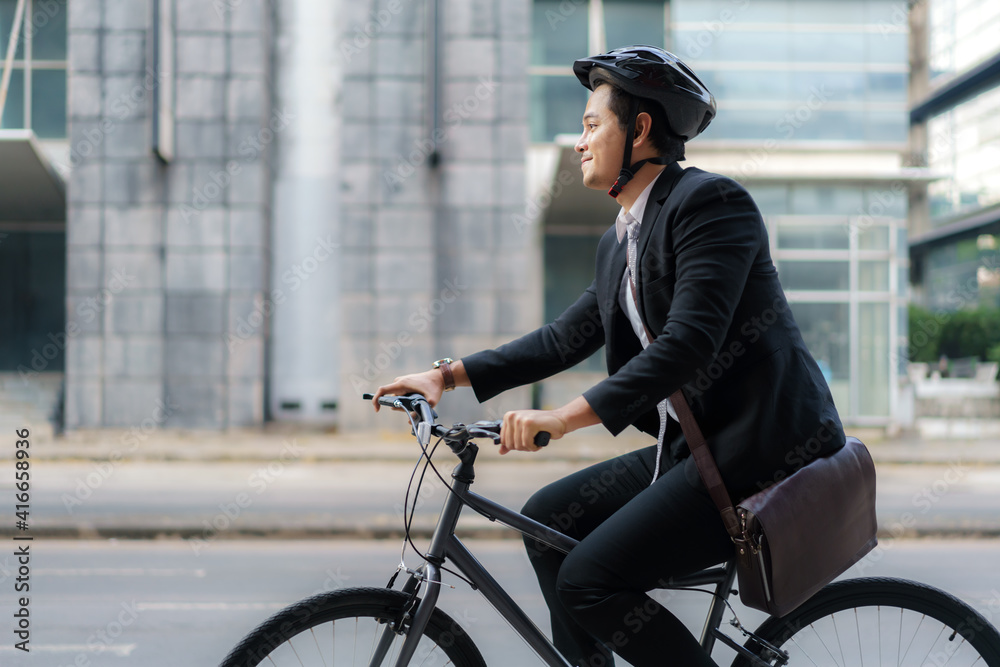 Asian businessman in a suit is riding a bicycle on the city streets for his morning commute to work.