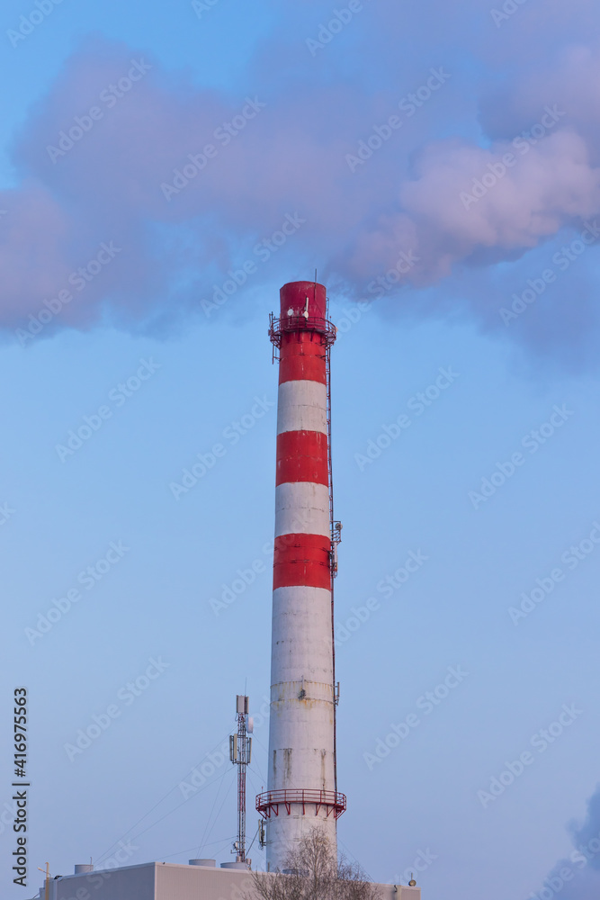 一家工厂红白相间的烟囱，在阳光明媚的日子里，灰色的烟雾在蓝天的映衬下冒出来。