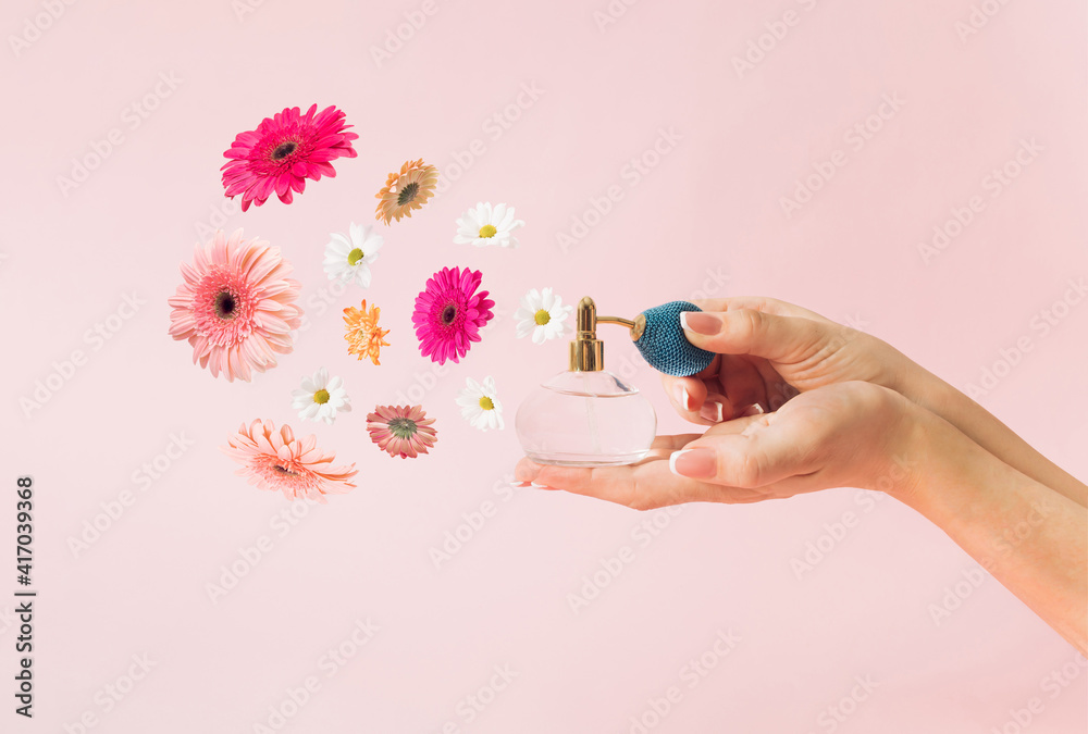 美丽的女性手拿着一种香水，从中开出各种各样的春花。粉红色的背景。