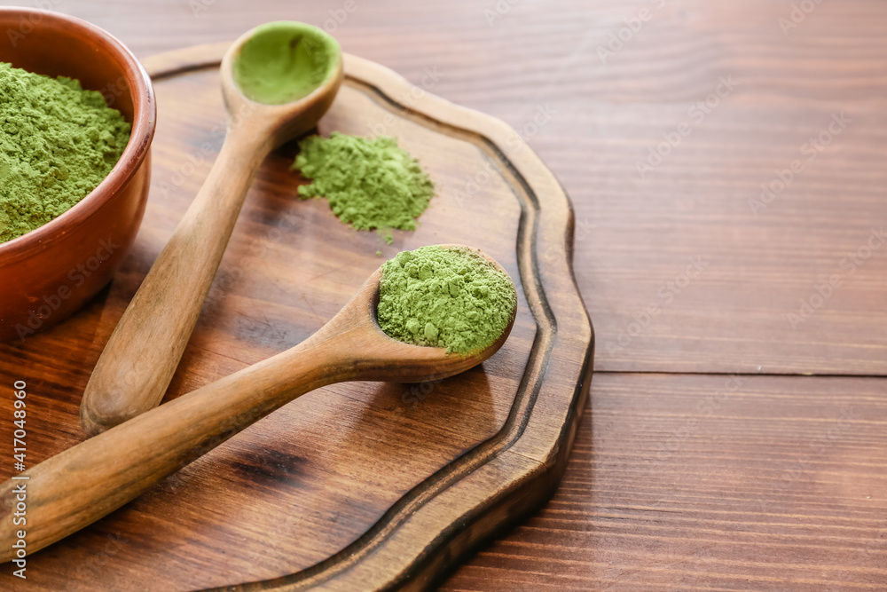 Spoons with powdered matcha tea on wooden background