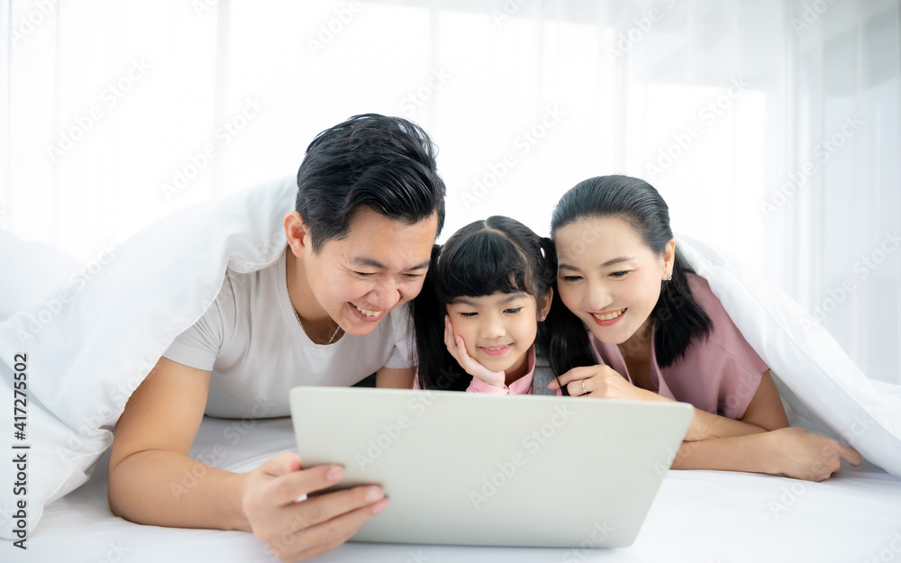 快乐的亚洲家庭人们一起在卧室里休闲。爸爸和妈妈带着女儿放松和
