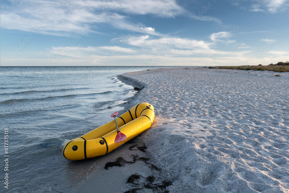 Yellow packraft rubber boat with red padle on a sea coast. Packrafting. Active lifestile concept