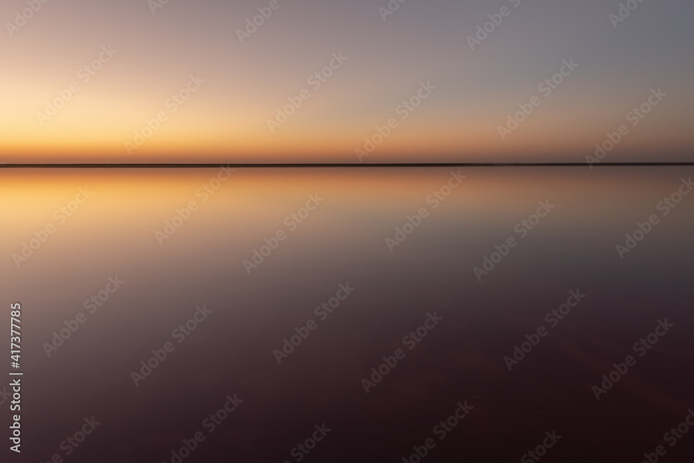 Tranquil minimalist landscape with smooth surface of the pink salt lake with calm water with horizon