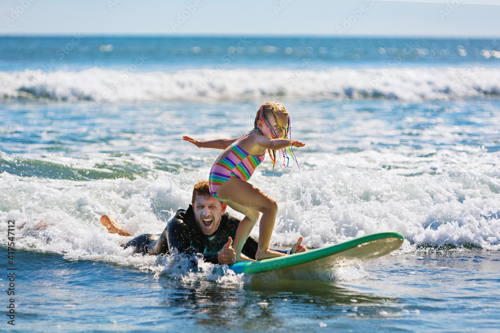 Little surf girl - young surfer learn to ride on surfboard with instructor at surfing school. Active