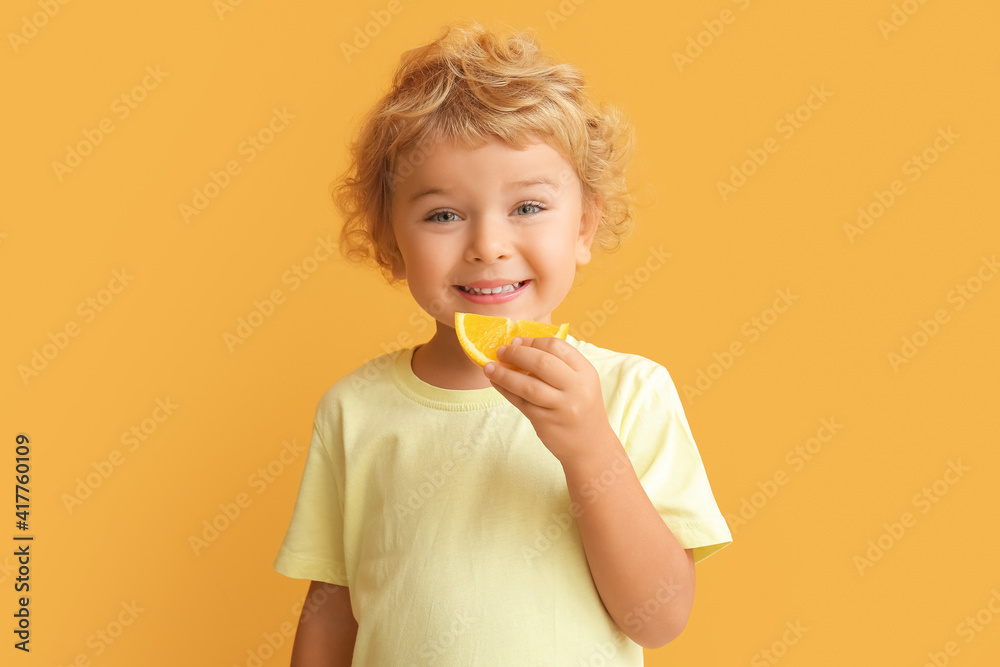 可爱的小男孩在彩色背景下吃橙色